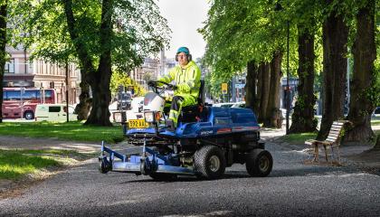 Kunnossapitotyöntekijä ajamassa ruohonleikkuria puistokäytävällä.