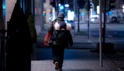 Nainen mustassa takissa ja mustissa housuissa kävelee jalkakäytävällä yöllä.