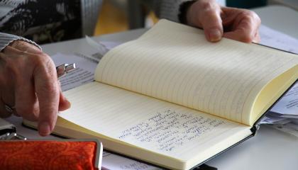 Avoinna oleva päiväkirja, jota kädet pitelevät.