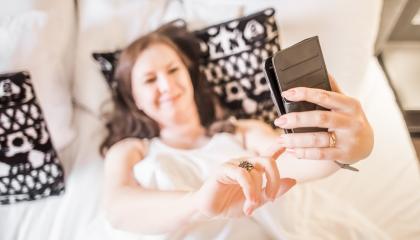 Sängyllä makoileva nainen ottaa kuvaa itsestään puhelimella.