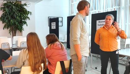 Kuvassa kaksi ihmistä keskustelemassa, opiskelijoita taustalla