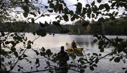 Kuvaaja seisoo vedessä ja soutaja soutaa.