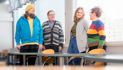 Neljä henkilöä seisoo pulpettien ääressä ikkunan vieressä.