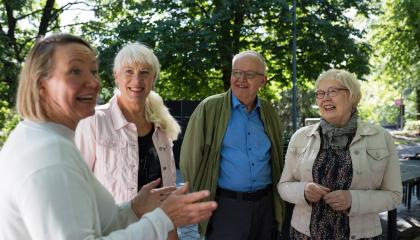 Neljä senioria keskustelee vilkkaasti ulkona Koskipuistossa.