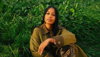 Nainen istuu vehreässä ruohikossa.