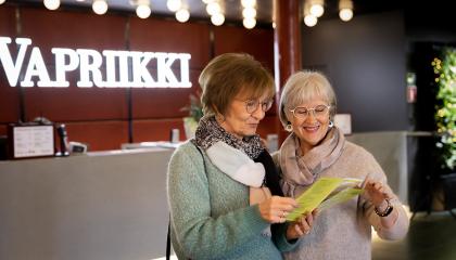 Kaksi eläkeläisnaista katselee Vapriikin esitettä museon aulassa. 