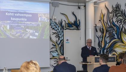 Pormestari Kalervo Kummola puhujakorokkeella kertomassa diaesityksen avulla vuoden 2025 talousarvion pääkohtia.