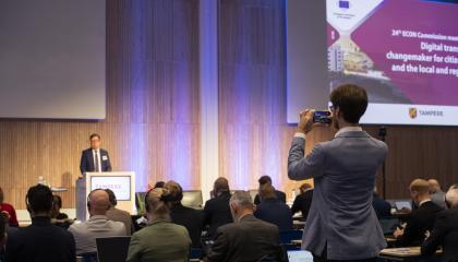 Mies ottamassa puhelimella kuvaa puhujasta konfrenssissa.