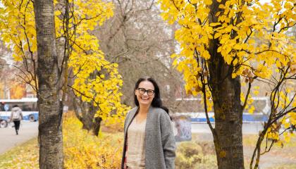 Hymyilevä henkilö kahden puun välissä. Puissa keltaiset lehdet.