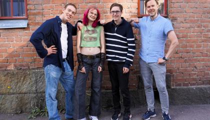 Kuvassa neljä henkilöä tiilimuurin edessä