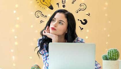 Henkilö istumassa tietokoneen ääressä. Hänen pään yläpuolelle on piirretty kysymysmerkkejä ja yksi hehkulamppu.