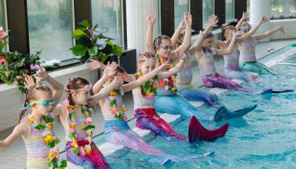 Tyttöjä uima-altaan reunalla vedenneitoasuissa.