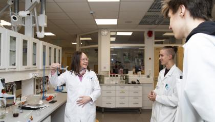 Kolme henkilöä seisoo laboratoriossa päällään valkoiset työtakit.