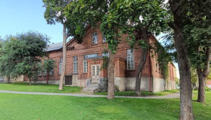 Vanha ja iso punatiilinen rakennus puiston keskellä.