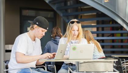 Lukion opiskelijat istuvat pöydän ääressä ja tekevät töitä tietokoneilla.