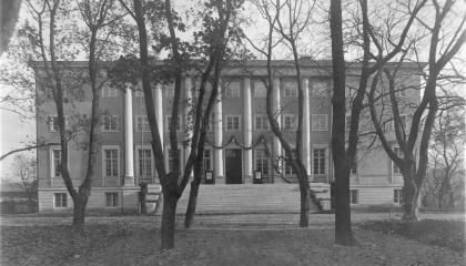 Mustavalkoisessa valokuvassa on iso klassinen rakennus keskellä puistoa.