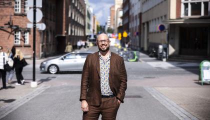 Mies seisoo kadulla hymyillen ja katsoo kameraan. 