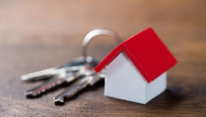 Avainnippu pöydällä ja avainperäksi on liitetty pieni punakattoinen valkoseinäinen mökki.