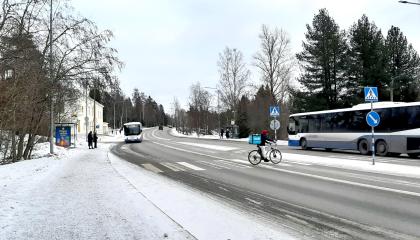 Kuvassa katua, busseja ja bussin odottajia, pyörälijä.