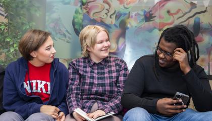 Kolme nuorta istumassa, keskimmäisellä kädessä kirja.