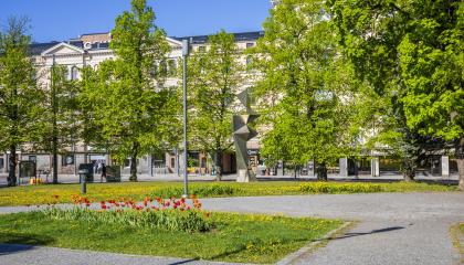 Kuvassa vihreää puistoa, käytäviä, tulppaaneja ja taideteos.