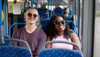 Tyttö ja poika bussissa, aurinkolasit silmillä.