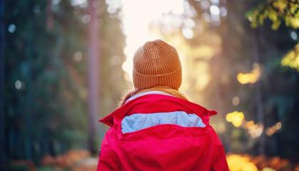 Nuori kävelee metsässä kohti auringonvaloa. Hänellä on oranssi myssy ja punainen takki.