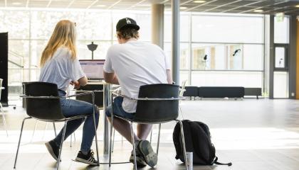 Kaksi opiskelijaa istuu pöydän ääressä koulun aulassa.