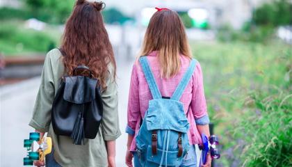 Kaksi nuorta kävelemässä poispäin katsojasta. Kummallakin on pitkät ruskeat hiukset ja kädessään skeittilauta.