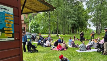 Ihmisiä istuu ruokaa nurmikolla.