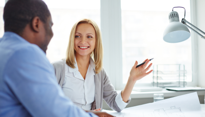 Kaksi henkilöä istuvät pöydän ääressä. He hymyilevät toisilleen ja keskustelevat.