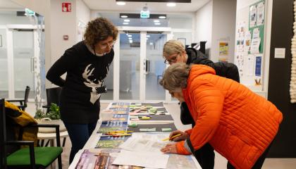 Kaupungin asiantuntija ja kaksi tamperelaista ovat kumartuneena yhdessä tutkimaan pöydällä olevaa asiakirjaa.