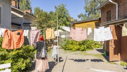 Pyykkejä roikkuu narulla Amurin museokorttelin pihalla kesäpäivänä. Aikuinen ja lapsi kulkevat pyykkien alta.