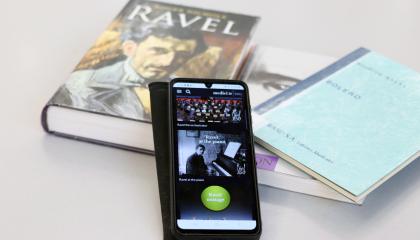 Älypuhelin nojaa kirjapinoon. Puhelimen näytöllä on avoinna videopalvelu, jossa voi katsoa konsertteja.