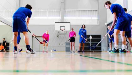 Lukio-opiskelijat pelaavat salibandya koulun liikuntasalissa. 