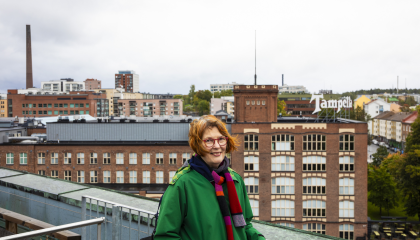 Henkilö seisoo kattoterassilla takanaan punatiilinen Tampellan vanha tehdasrakennus, jossa on iso Tamperella-kyltti katolla.