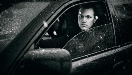 Mustavalkoisessa kuvassa Harry-Pekka on sateisen auton sisällä, etuoven lasi auki.