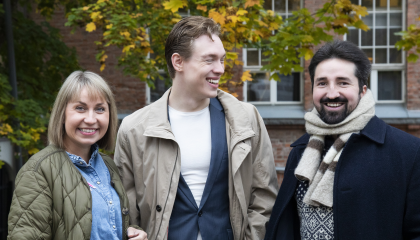 Kolme henkilöä seisoo syksyisen värikkään puun edessä.