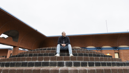 Henkilö istuu punatiilisen rakennuksen edessä portailla.