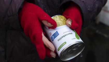 Hernekeittopurkki ja ihmisen kädet, joissa on punaiset rikkinäiset kangashansikkaat.