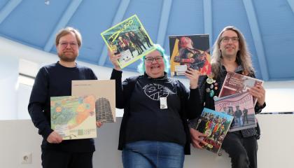Kolme henkilöä seisoo iloisena vinylilevyjä käsissään.