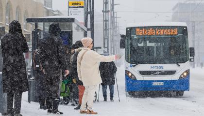 Talvisella pysäkillä nainen pysäyttää bussin, jossa lukee: Matkalla kanssasi.