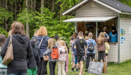 Ihmisiä jonottamassa puiseen koppiin, josta kaksi nuorta jakaa ruokaa.