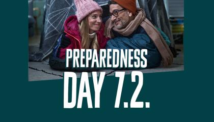 A warmly dressed woman and man smile at each other in a picture with the words "Preparedness Day 7.2." written on it.