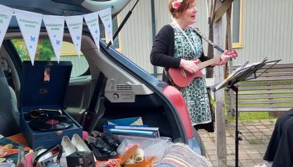 Nainen soittaa ukulelea kukkaseppele päässään ja laulaa yleisölle.