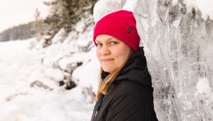 Punapipoinen henkilö nojaa jäiseen korkeaan kallioon.