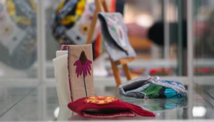 Vitriini, jossa on kirjontatöitä. Etualalla kukka-aiheinen työ.