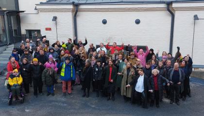 Noin 60 ihmistä ryhmäkuvassa vanhan rakennuksen edustalla. 