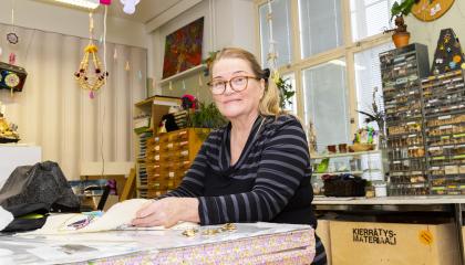Raitapaitainen nainen tekee käsityötä Monitoimitalon kädentaitopajassa.