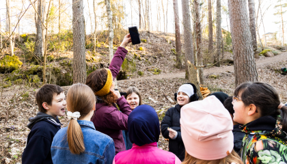 Aikuinen pitää kädellään desibelimittaria korkealla ilmassa ja lapset seuraavat tilannetta ympärillä.